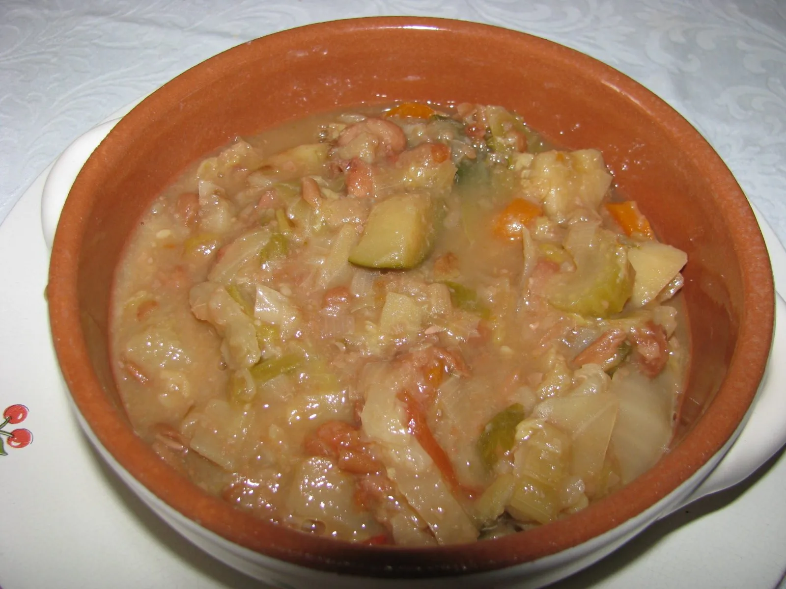 Ciotola di terracotta con ribollita toscana di verdure, fagioli e pane, appoggiata su un piatto bianco